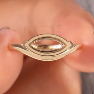 May include: A gold ring featuring a marquise-shaped setting designed to hold a gemstone. The metal band has a smooth, polished finish with geometric detailing surrounding the central open frame, creating a sleek and structured appearance.