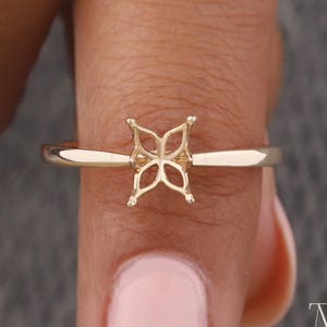 Op de afbeelding: Een goudkleurige ring met een vier-klauwzetting. De ring heeft een dunne, gladde band en de zetting is ontworpen om een edelsteen vast te houden. De ring wordt op een vinger getoond tegen een neutrale achtergrond. De ring is een fijn sieraad.
