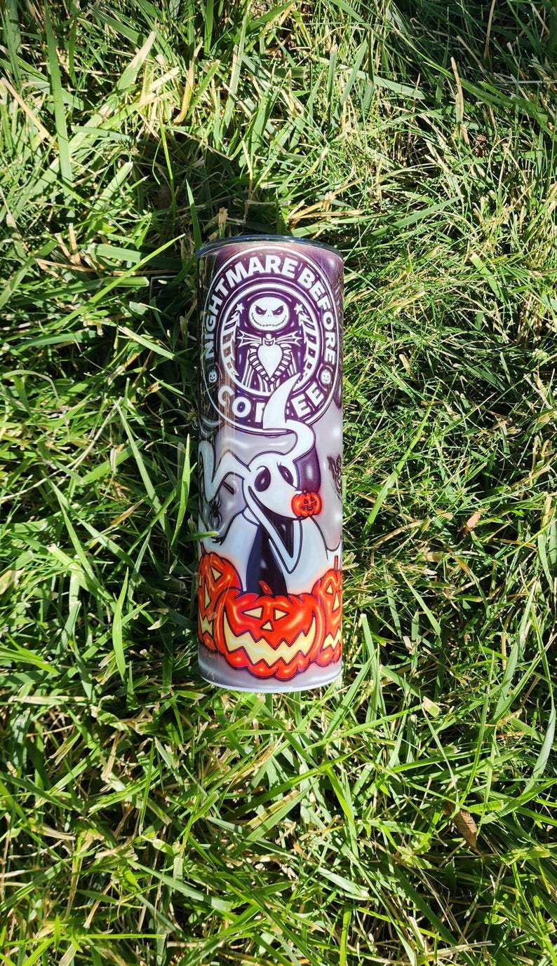 May include: A white stainless steel tumbler with a Nightmare Before Christmas design. The design features Jack Skellington, Zero the ghost dog, and pumpkins. The text "Nightmare Before Coffee" is printed on the tumbler.