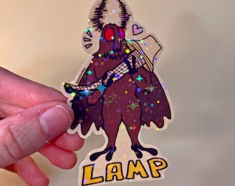 May include: A holographic sticker of a brown moth with red eyes holding a lamp. The moth is surrounded by a glittery background with stars and the word "LAMP" is written below the moth.