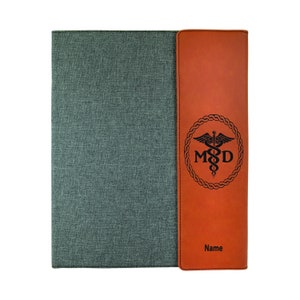 May include: A brown leatherette folder with a gray fabric cover. The folder has a pocket on the right side with a medical symbol and the letters "M.D." engraved on it. The folder also has the word "Name" printed on the pocket.