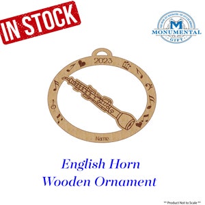 May include: A wooden ornament shaped like an English horn with musical notes around the edge. The ornament is brown and has the year 2023 and the word "Name" engraved on it. The ornament is a Christmas decoration.