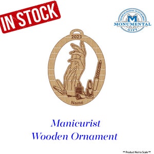May include: A wooden Christmas ornament shaped like an oval with a design of hands getting a manicure. The ornament is brown and has the year 2023 and the word "Name" engraved on it.
