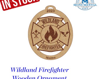 May include: A wooden ornament shaped like a firefighter's cross with the words "Wildland Firefighter" and "2023" on it. The ornament is brown and has a red flame design in the center.