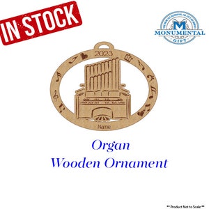 May include: A wooden ornament shaped like an organ with musical notes around the edge. The ornament is brown and has the year 2023 on it. The text "Organ Wooden Ornament" is below the ornament.