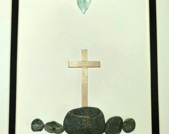 Könnte beinhalten: Gerahmtes Kunstwerk mit einem Holzkreuz und einem herzförmigen Stück Meeresglas über einer Ansammlung von Steinen. Der Text "John 3:16" ist darunter geschrieben. Das Kunstwerk ist mit einem schwarzen Rahmen versehen.