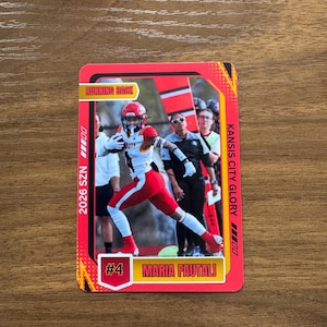 May include: A rectangular sports trading card featuring a football player in a red and white uniform with the text RUNNING BACK, 2026 SZN, KANSIS CITY GLORY, #4, and MARIA FAUTALI. The card has a bright red border with yellow accents and graphic details.