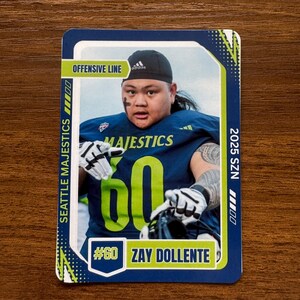 May include: A football trading card featuring Zay Dollente, number 60, of the Seattle Majestics. The card has a blue and green color scheme with the text "OFFENSIVE LINE" and "2025 SZN". The player is wearing a navy blue jersey.