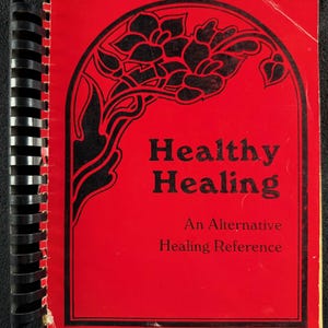 Puede incluir: Un libro encuadernado en espiral rojo con el título "Healthy Healing" en letras negras. La portada presenta un diseño floral negro y el subtítulo "An Alternative Healing Reference".