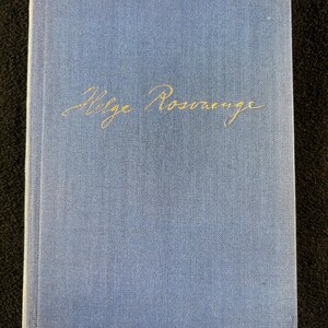 May include: A hardcover book with a light blue cover. The title "Helge Rosmerge" is written in gold script across the front. The book has a textured appearance and a slightly worn look.
