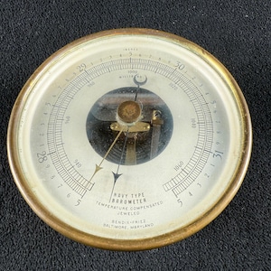 May include: A white ceramic mug with a black handle and the text "But First, Coffee" in a bold, black font. The mug is set against a blurred background, suggesting a cozy setting.