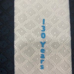 May include: A white fabric with a black stripe on the left side and a blue vertical stripe on the right side. The blue stripe has the text "130 Years" printed on it.