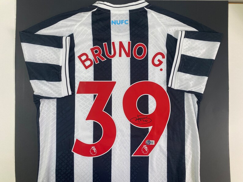 May include: A white and black striped soccer jersey with the name "BRUNO G." and the number "39" on the back. The jersey has the team logo and the text "NUFC" on the back.