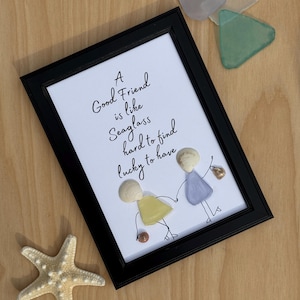 May include: A framed artwork with a white background and black text that reads "A Good Friend is like Seaglass hard to find lucky to have". The artwork features two figures made of seashells, holding hands.