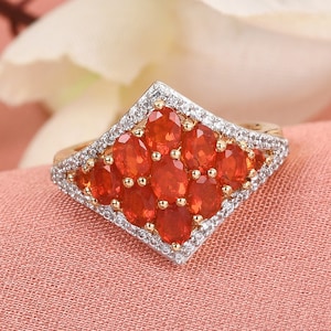 May include: A gold ring with a diamond-shaped setting featuring a cluster of orange gemstones surrounded by smaller white gemstones.