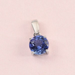 May include: A silver pendant with a round, blue gemstone set in a prong setting.