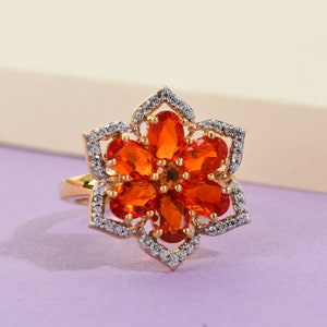 May include: A gold ring with a flower design featuring orange gemstones and clear stones. The ring is set on a purple background.