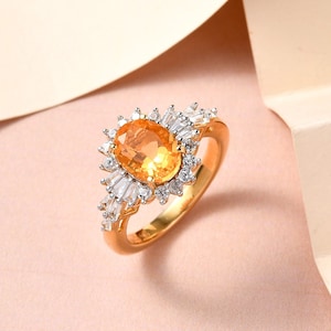 May include: A gold ring with a large oval-shaped orange gemstone surrounded by smaller white gemstones.