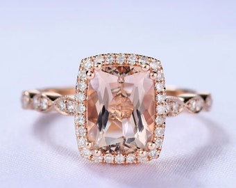 May include: A rose gold engagement ring with a cushion-cut morganite center stone surrounded by a halo of smaller diamonds. The band is a delicate twisted design with pave diamonds.
