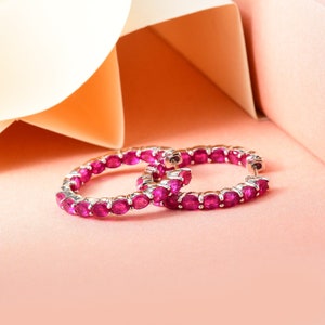 May include: A pair of silver hoop earrings with a row of pink ruby stones around the entire hoop.