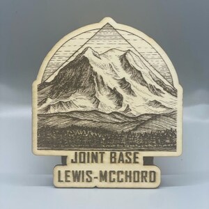 May include: A wooden sign with a mountain range illustration and the text "Joint Base Lewis-McChord".