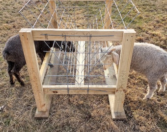 May include: A wooden and wire livestock feeder with two sheep. The feeder is constructed with wooden beams and wire mesh, designed to hold hay or feed. The sheep are positioned on either side of the feeder, eating.