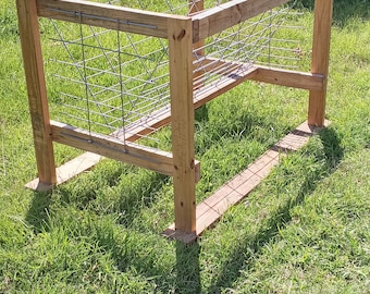 May include: A wooden frame with a wire mesh insert, likely used for feeding livestock. The frame is sitting on a grassy lawn.