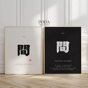 May include: Two framed art prints with gold frames. One print has a white background with black Japanese characters and the text "THE SPACE BETWEEN". The other print has a black background with white Japanese characters and the text "THE SPACE BETWEEN".