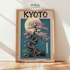 May include: A framed poster featuring a stylized illustration of a cherry blossom tree in Kyoto, Japan. The artwork includes the word "KYOTO" in large black letters, a full moon, and Japanese text. The poster is in a wooden frame.
