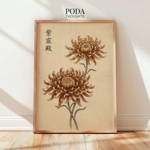 May include: Framed botanical print featuring two detailed brown chrysanthemum flowers with green stems against a beige background. The print includes Japanese characters and the text "PODA THOUGHTS" at the top. The frame is a light brown color.
