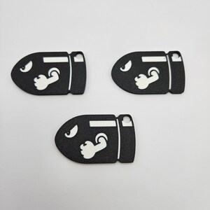 May include: Three black and white bullet bill keychains with a white eye and arm design.