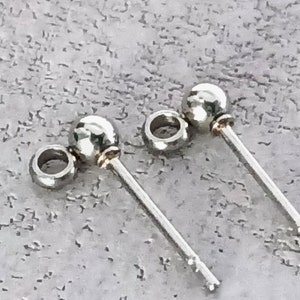 May include: Two silver earring posts with small round balls at the top. The posts are approximately 2.5 cm long.