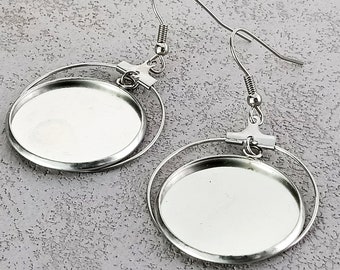 Può includere: Un paio di orecchini d'argento con montature rotonde a schienale aperto. Le montature sono progettate per contenere un pezzo piatto e rotondo di vetro o altro materiale.