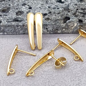 Könnte beinhalten: Vier goldfarbene Ohrring-Verschlüsse. Zwei sind gerade, zwei sind gebogen. Die geraden Verschlüsse haben ein spitzes Ende und eine Öse am anderen Ende. Die gebogenen Verschlüsse haben an jedem Ende eine Öse.