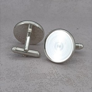 May include: A pair of silver cufflinks with round, blank, silver-toned, circular inserts. The cufflinks have a simple, classic design.