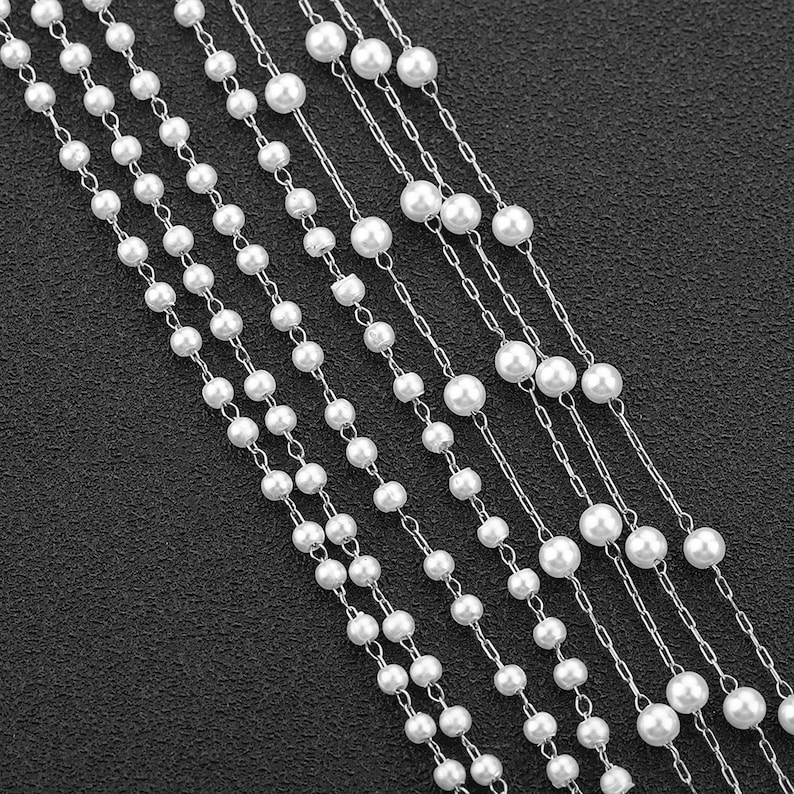 May include: A multi-strand necklace featuring white faux pearls and silver chains. The necklace is layered and creates a cascading effect.