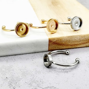 May include: Three adjustable ring blanks with round bezel settings. The bezels are silver, gold, and rose gold. The rings are made of metal.