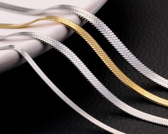 May include: Four silver and gold snake chain necklaces on a white surface. The chains are arranged in a staggered pattern, with the gold chains on top of the silver chains.