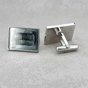 Puede incluir: Un par de gemelos de plata. Un gemelo tiene un diseño rectangular texturizado. El otro gemelo tiene un diseño rectangular liso con una barra de plata que conecta a un botón redondo.