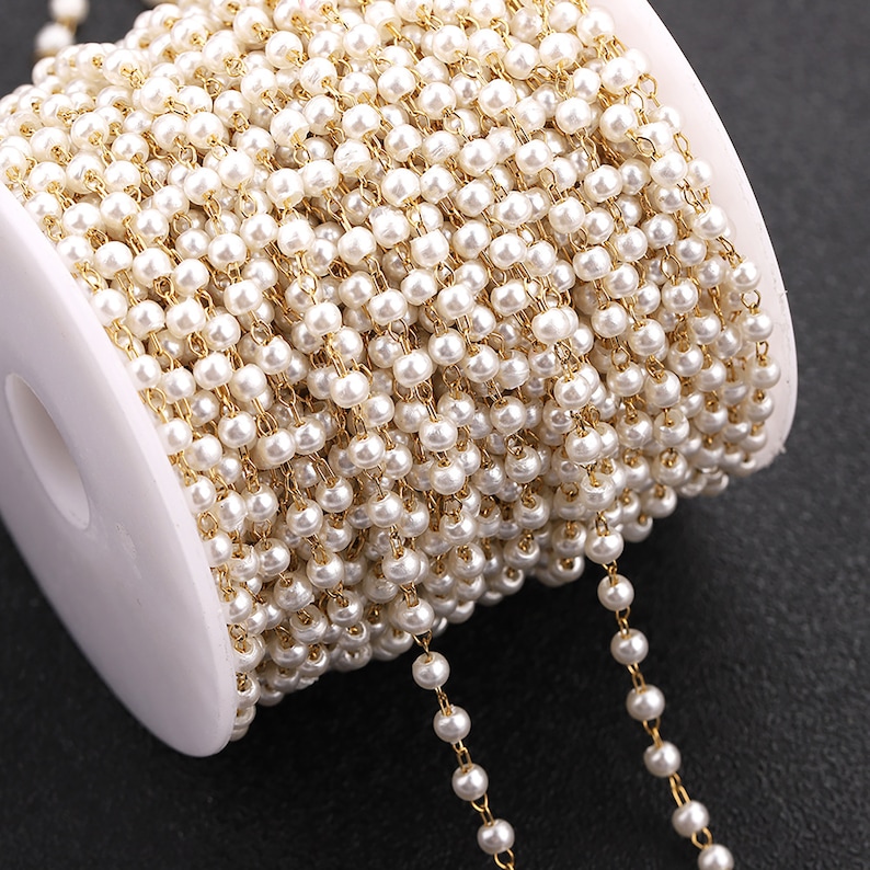 May include: A spool of gold chain with white pearl beads. The chain is wound around a white spool.