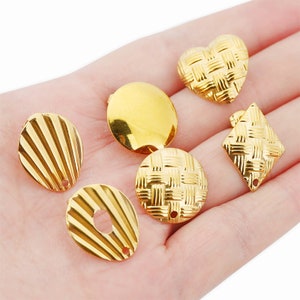 Puede incluir: Seis abalorios de metal de color dorado con diferentes diseños. Los abalorios incluyen un corazón, un círculo, un cuadrado y tres formas de concha diferentes.