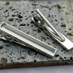 以下が含まれることがあります： 2つのシルバーのネクタイピン。1つは長方形のデザイン、もう1つはより伝統的なデザイン。どちらも磨かれた金属製で、洗練されたモダンな外観です。