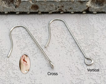 May include: Three silver earring hooks, one with a cross shape, one with a vertical loop, and one with a curved hook. The hooks are shown on a textured gray surface.