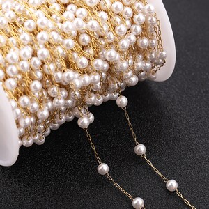 May include: A spool of gold chain with white pearl beads strung on it. The chain is unraveled and shows the beads and chain detail.