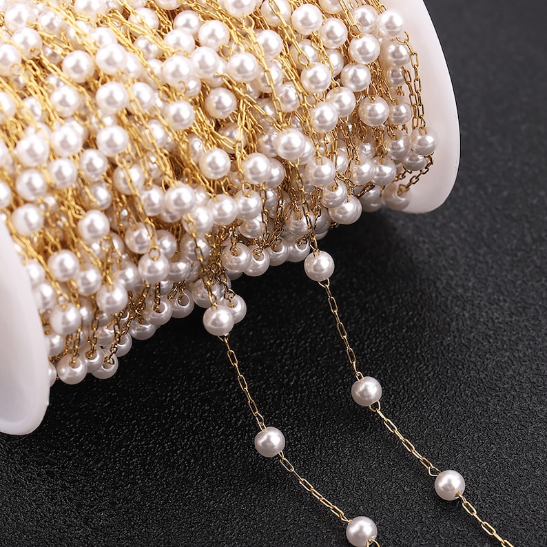 May include: A spool of gold chain with white pearl beads strung on it. The chain is unraveled and shows the beads and chain detail.