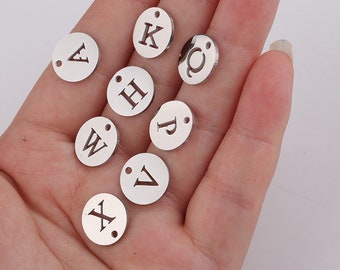 May include: A collection of silver metal letter charms with a hole for attaching to jewellery or other crafts. The letters include A, C, H, K, P, V, W, and X.