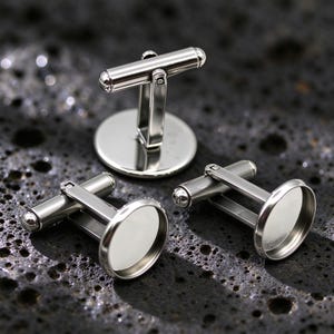 May include: Three silver-toned metal cufflinks featuring a circular bezel setting. Each cufflink has a polished finish, a hinged T-bar toggle mechanism, and a flat, round face designed to hold an insert or cabochon for decorative purposes.