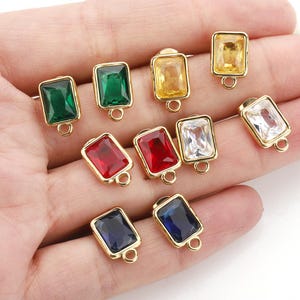 May include: Assortment of ten gold-toned metal charms with colourful square-shaped glass stones. Each charm has a loop for attaching to jewellery or other crafts.
