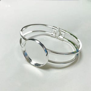 May include: Silver bangle bracelet with a round, clear glass bezel. The bracelet is double-layered and has a hinged clasp.