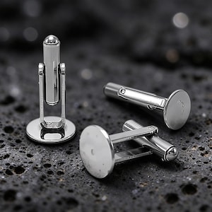 May include: Three silver-toned metal cufflinks featuring a circular flat face and a hinged toggle mechanism. The polished metallic surfaces reflect light, showcasing a smooth, reflective finish on the round fronts and the cylindrical posts.